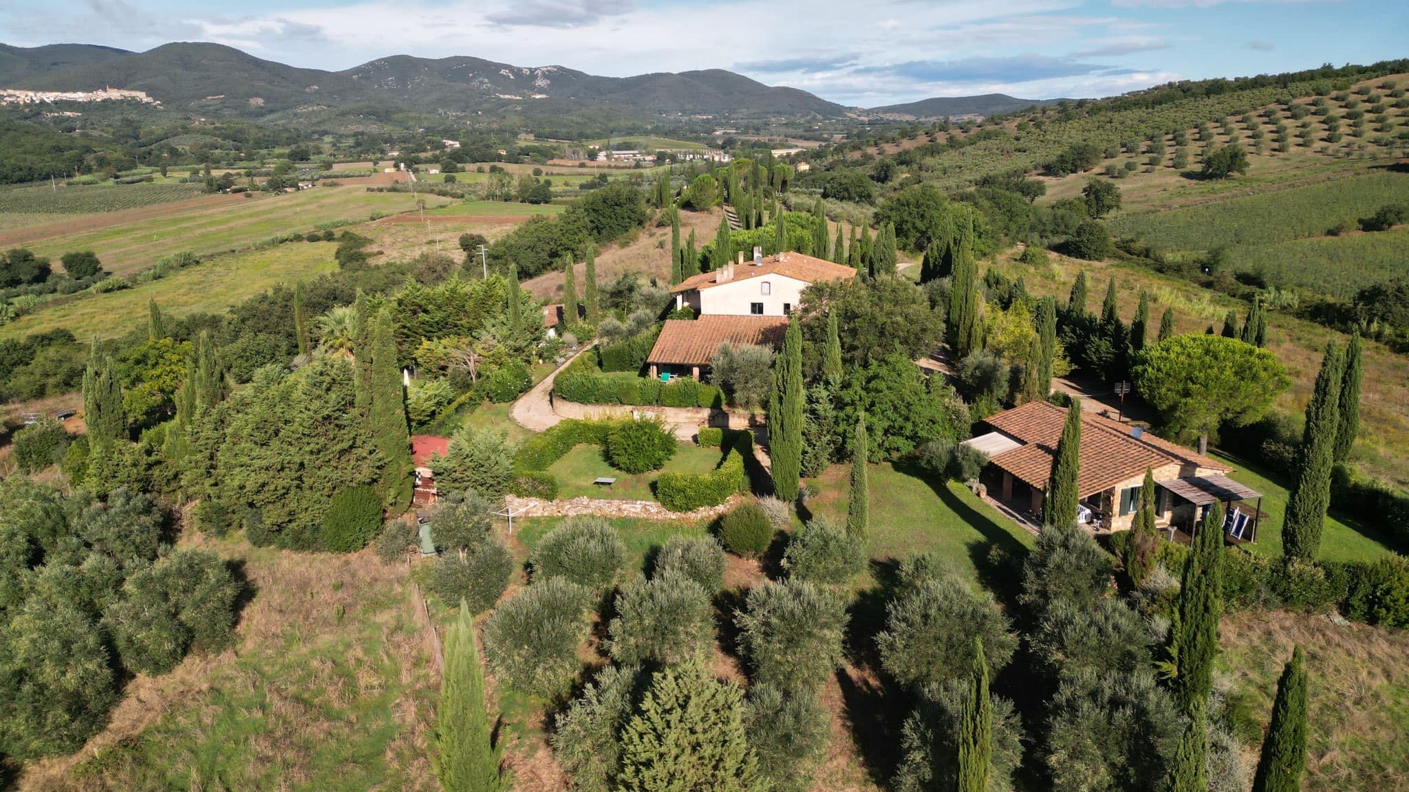 Luftaufnahme der Anlage über den Hügeln der Maremma, mit Haupthaus, Zypressen und Schwimmbad