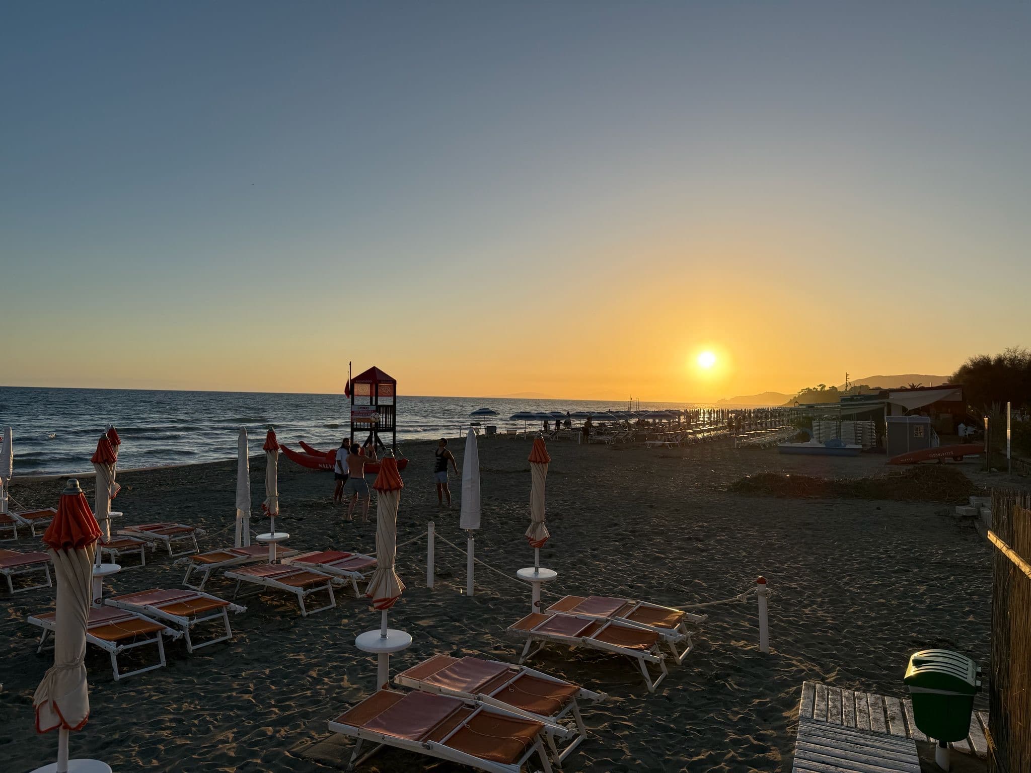 Sonnenliegen und Schirme am Strand bei Sonnenuntergang